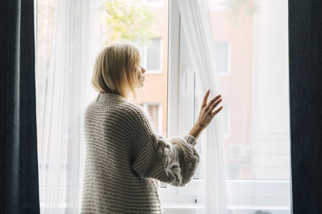 冠状病毒大流行期间忧郁女人在家的侧视图透过窗户看预防Covid19空间