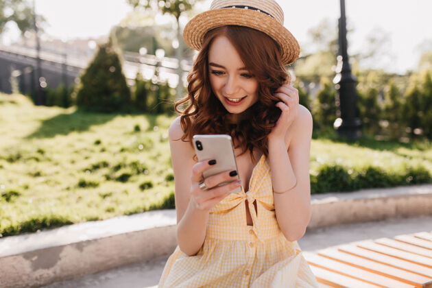 公园惊艳的姜女青年在公园里看了一条电话留言一张穿着黄色连衣裙的可爱优雅女孩坐在长椅上拿着智能手机的户外画像浪漫阳光现代