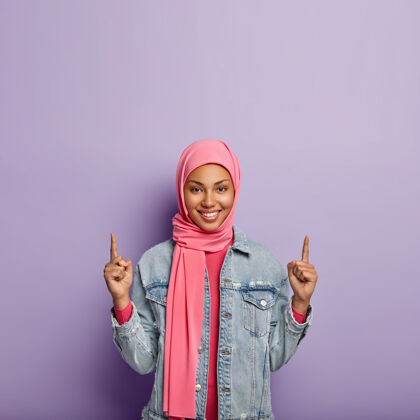 头巾伊斯兰时尚概念高兴积极的女性与特定的外观和服装 点以上的自由空间 向上显示一些东西 穿时尚夹克女孩在头巾广告对象上牙齿空白自由空间