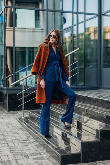 成功了可爱时尚的女人带着走在都市商业街上的温暖棕色外套和蓝色西装 春秋时尚的街头风 戴着墨镜