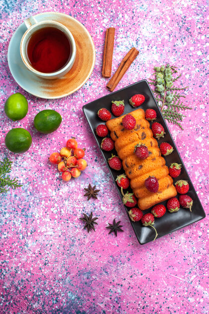 烘焙顶视图美味的烤蛋糕放在红色的蛋糕锅里 粉红色的桌子上放着新鲜的红色草莓茶和柠檬水果饼干烘焙