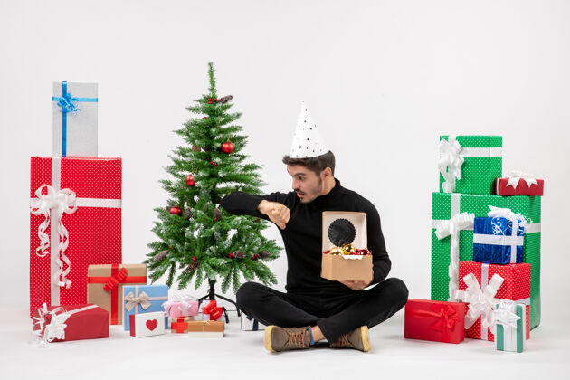 前面前视图：年轻人围坐在节日礼物旁 手里拿着树上的玩具 在白墙上查看时间时间玩具人
