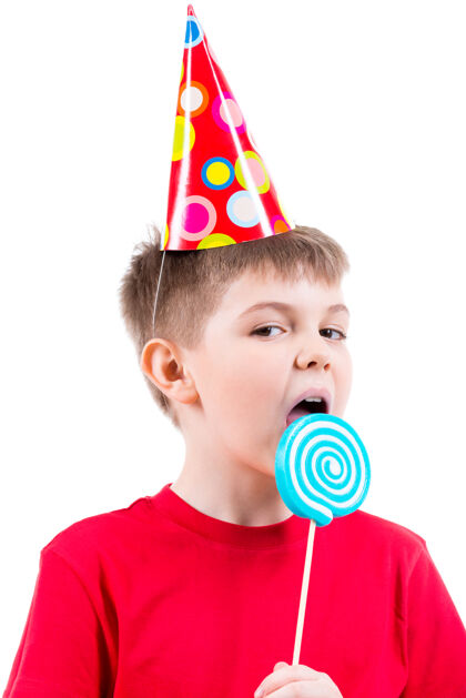 甜食穿着红色t恤 戴着派对帽 吃着彩色糖果的小男孩-被隔离在白色衣服上玩耍庆祝表情