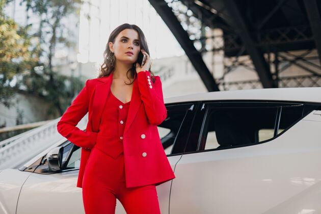 交谈穿着红西装的性感美女在车前摆姿势打电话谈生意穿着优雅燕尾服