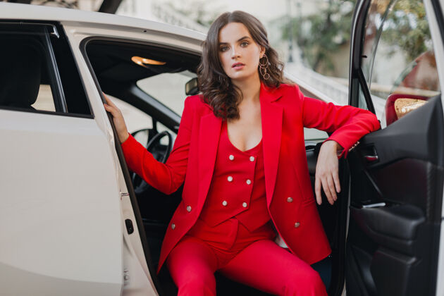 燕尾服穿着红西装的性感富商美女在白色汽车里摆姿势时尚衣服女性