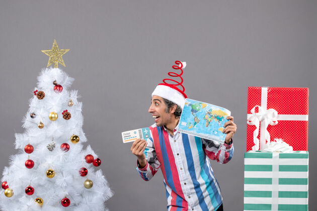 票正面图快乐的男人戴着螺旋弹簧圣诞帽拿着世界地图和旅行票看着右边地图人看