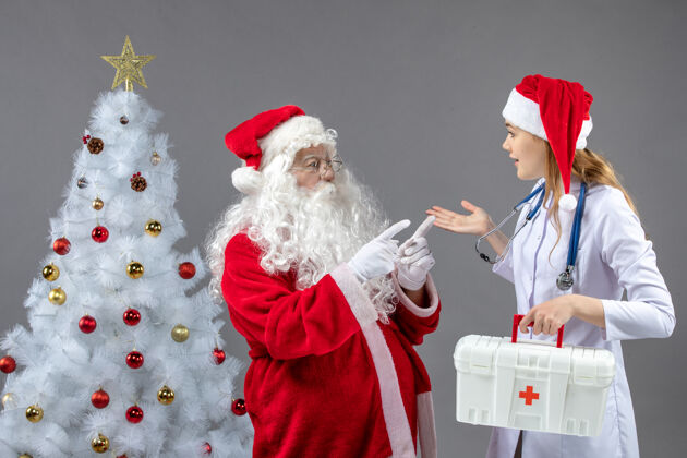 举行圣诞老人和女医生的前视图 女医生拿着急救箱在灰色的墙上医生快乐人