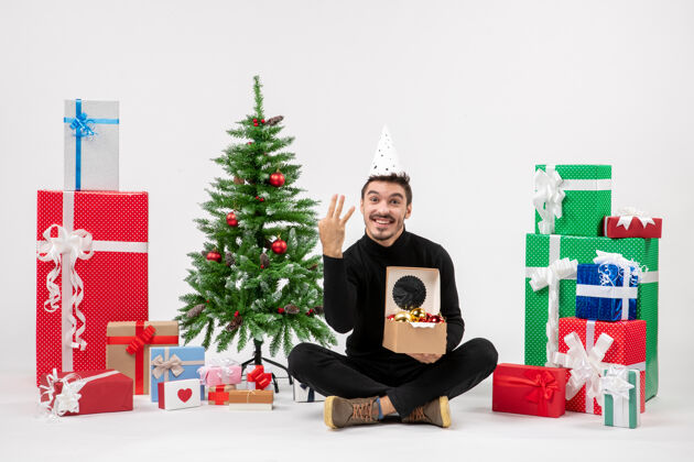 礼物正面图：年轻人围坐在白色的墙上 手里拿着圣诞礼物盒子坐着人