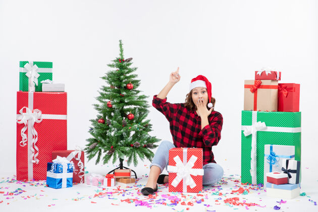 礼物年轻女子围坐在礼物和白色墙上的小圣诞树前的视图圣诞快乐圣诞快乐