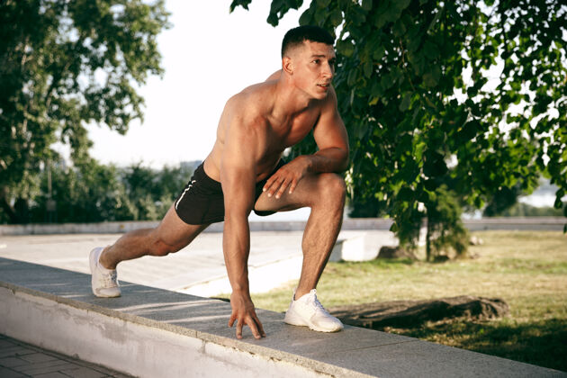 男性一个肌肉发达的男运动员在公园里锻炼体操 训练 健身锻炼 柔韧性夏日城市在阳光明媚的日子背景场上积极健康的生活方式 青春 健美成人人健康