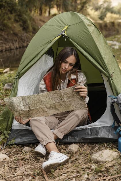 露营快乐的野营女孩在森林里查看地图前视图露营度假体验
