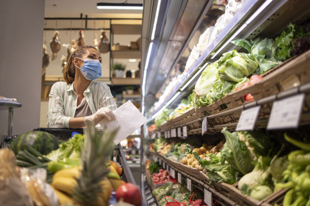 保健戴着卫生口罩 橡胶手套和购物车的妇女在杂货店买蔬菜 准备进行冠状病毒大流行隔离蔬菜超市购物