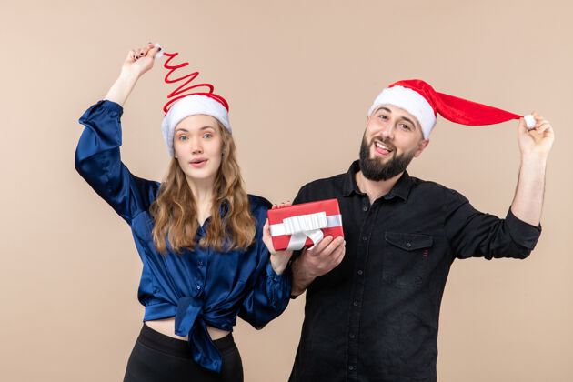 年轻前视图年轻夫妇都举行了一个粉红色的背景礼物节日照片新年圣诞礼物男性礼物服装帽子礼物