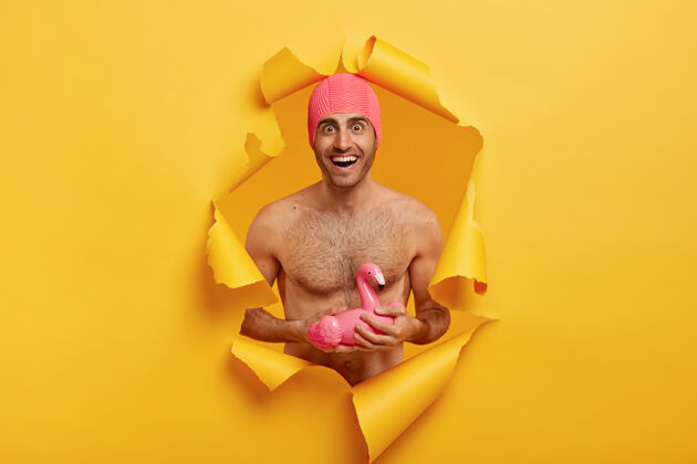 娱乐暑假的概念快乐的男人 良好的体形 赤裸的躯干站立 穿着粉色泳衣 手持充气火烈鸟携带停留家伙