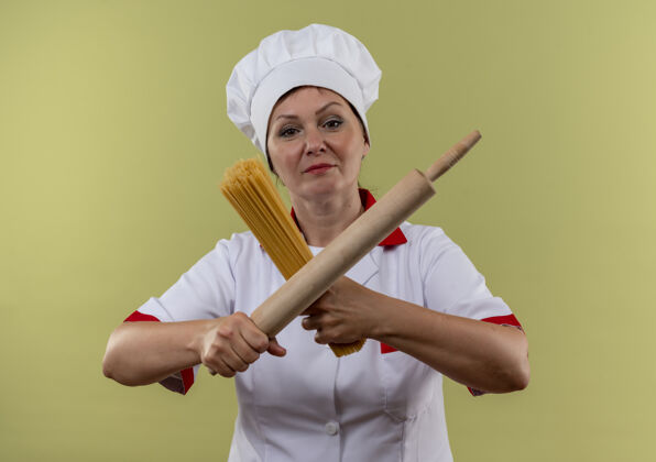 厨师身着厨师制服的中年女厨师手拿擀面杖和意大利面 在与世隔绝的绿墙上横穿别针厨师中年