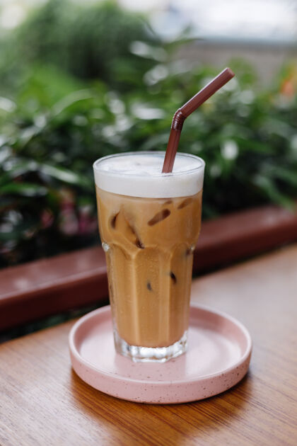 下午在绿色灌木丛的夏日咖啡馆里 粉红色的架子上放着一杯冰拿铁饮料卡路里咖啡