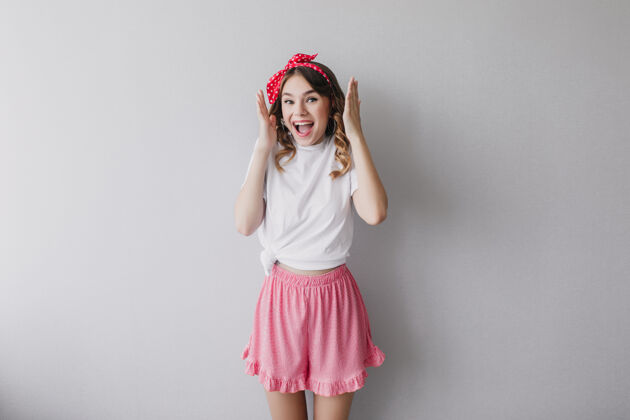 有趣快乐的女孩穿着可爱的粉色短裤摆出有趣的姿势室内照片是一位受白种人启发的卷发女士魅力快乐肖像
