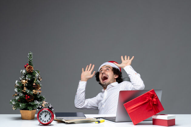 年轻商人新年的心情与震惊兴奋的年轻商人与圣诞老人的帽子坐在黑暗的背景办公室笔记本电脑圣诞老人生活