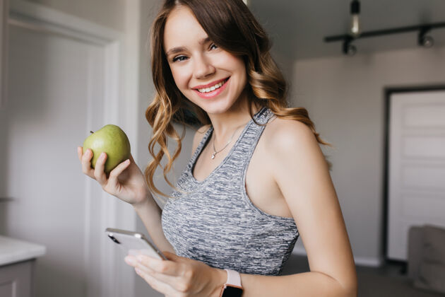 美丽苗条漂亮的女孩 波浪形的头发摆着手机和水果的姿势浪漫的女模特早上吃青苹果的室内写真家可爱营养