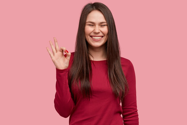 女性开朗的黑发亚洲女士用手做一个好的手势 笑容灿烂 脸上有雀斑 表示同意 穿红色衣服情绪亚洲人认可