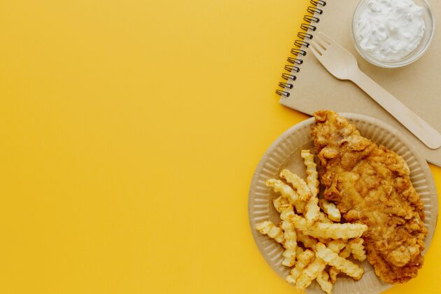 酱汁带笔记本和叉子的盘子上的鱼和薯条的俯视图美食菜英语