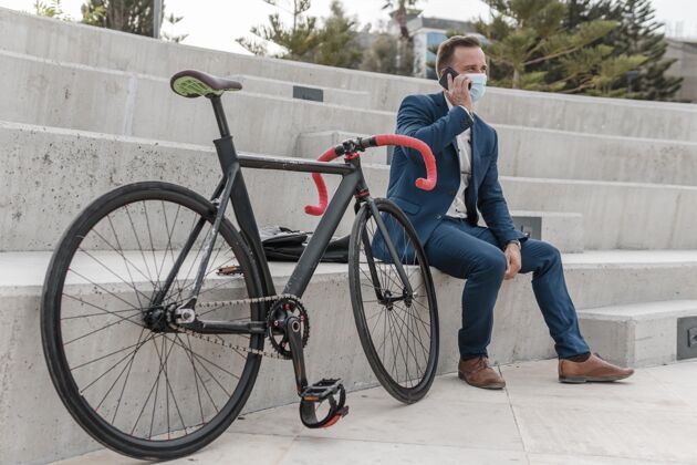 享受坐在自行车旁边戴着医用面罩的男人骑自行车的自行车运动的