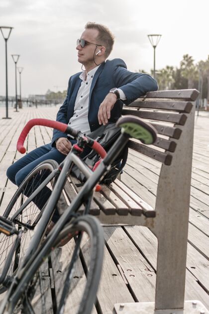 骑自行车的戴太阳镜的男人坐在自行车旁边的长凳上骑自行车的运动运动的