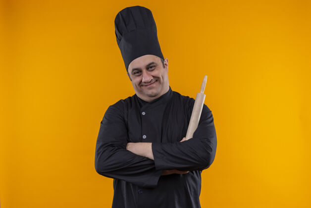 手高兴的中年男厨师穿着厨师制服 手拿擀面杖在黄墙上交叉厨师交叉抱