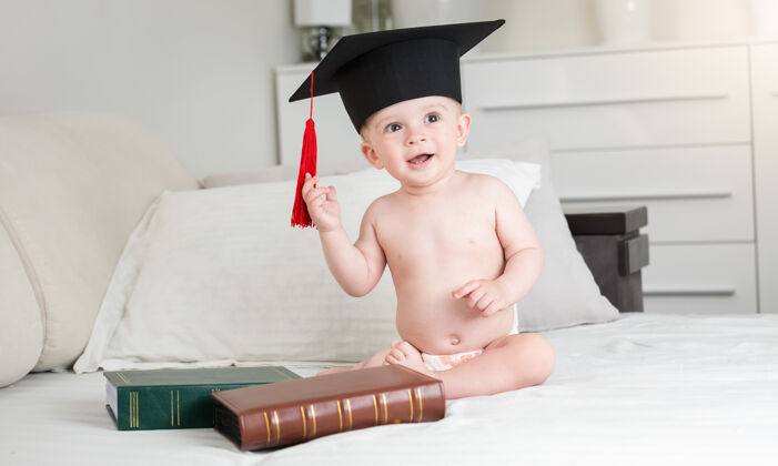 家庭穿着尿布 戴着黑色毕业帽的滑稽男婴的画像年轻知识尿布