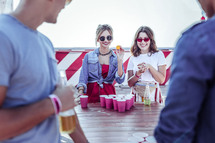 屋顶桌上游戏快乐的女孩脸上保持微笑 同时看着他们的合作伙伴啤酒互动社交