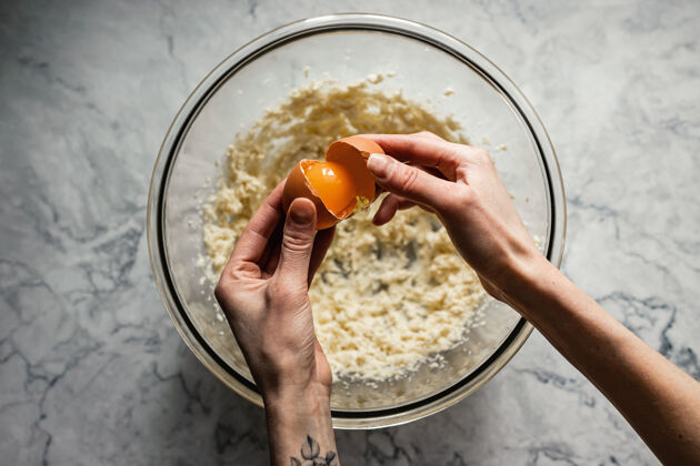 黄油烤饼干在一个大玻璃碗里把一个鸡蛋放进黄油和糖的混合物里俯视水平照片混合物开销准备
