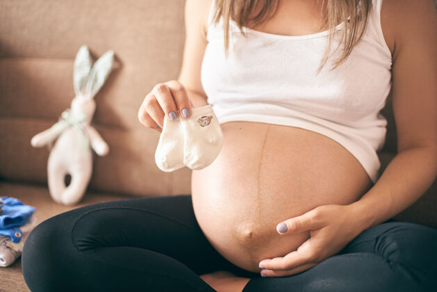 新的未来母亲的前视图 保存着宝宝的小袜子衬衫生活腹部