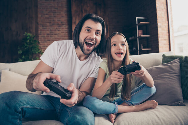 女孩美丽可爱的小女孩和英俊年轻的爸爸坐在舒适的沙发上的照片欢乐玩家视频游戏
