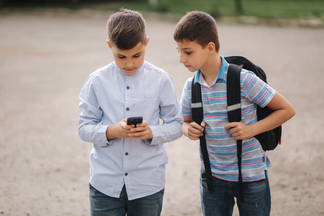 休闲两个男孩在隔离区玩网络游戏小男孩微笑着打电话一个看怎么玩另一个男孩朋友手机