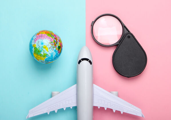 玩具旅游和旅游概念地球仪 放大镜和客机雕像上粉蓝色粉彩墙顶视图平躺乘客飞机旅行