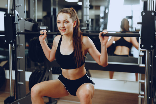 年轻年轻女子在健身器材里用杠铃做下蹲动作室内健身运动