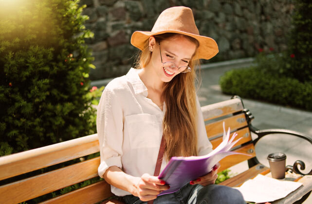 年轻年轻的白人女学生穿着休闲服 坐在公园的长椅上阅读文件夹中的esse积极卷发知识