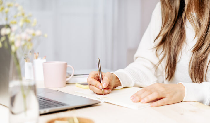 在线女人用笔记本在桌上的笔记本上写字远程室内学习