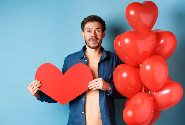 感情情人节的概念男人坠入爱河 惊愕地看着女友 露出一颗大红心 站在蓝色背景下的气球旁伴侣休闲礼物