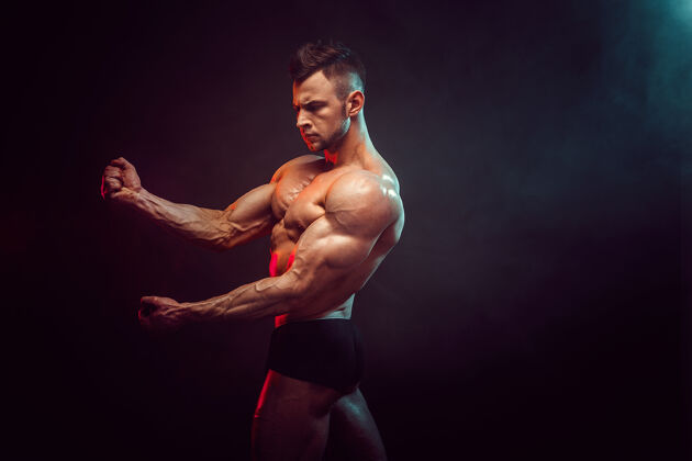 赤膊运动员在工作室里用烟在黑暗的墙上锻炼肌肉强壮的健美运动员拥有完美的腹肌锻炼男子健身