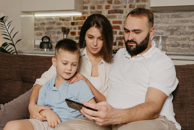 男孩晚上在家里 一位丈夫正在用智能手机向笑着的孩子和妻子演示这个节目男性孩子父母
