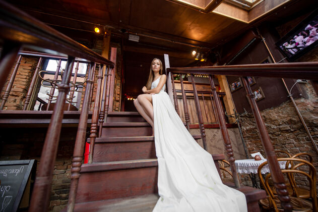 姿势穿着白色飘逸长裙的年轻优雅女孩在室内楼梯上摆姿势木头楼梯室内
