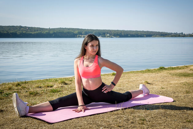 灵活白天 穿着运动服的年轻迷人的女人在湖边的草地上伸展热身绳健康的生活方式女孩健康锻炼