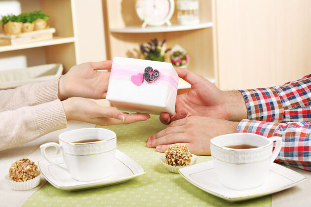 乐趣女性和男性的手与茶杯和礼品盒在家里糖果桌子配对