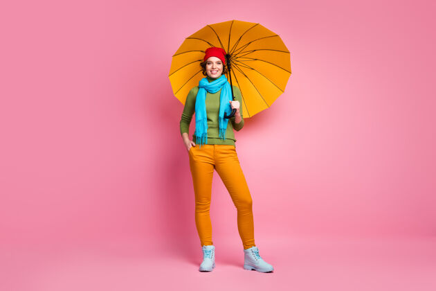 女性快乐女孩的全尺寸照片拿着她明亮的黄色阳伞享受季节自由时间旅行穿套头衫裤子鞋子隔着粉红色的墙颜色鞋子散步