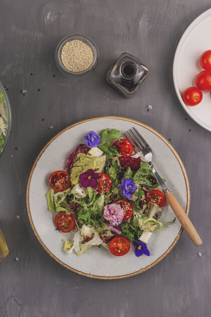 草药一张灰色的桌子上有西红柿 莴苣和奶酪的素食沙拉 上面点缀着可食用的花和配料春季食品概念乡村沙拉吃