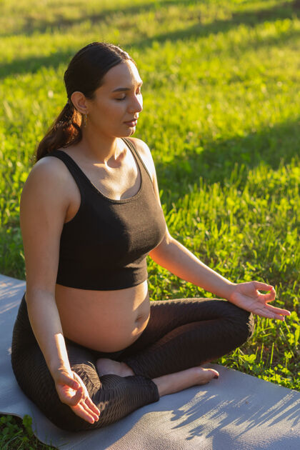 积极阳光明媚的日子里 可爱的年轻孕妇坐在草坪上的地毯上冥想自然健康女人