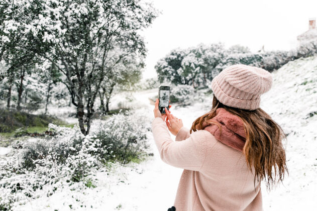 记忆一位穿着暖和外套的匿名女士站在树林里 一边用智能手机拍摄雪景的后景风景风景匿名