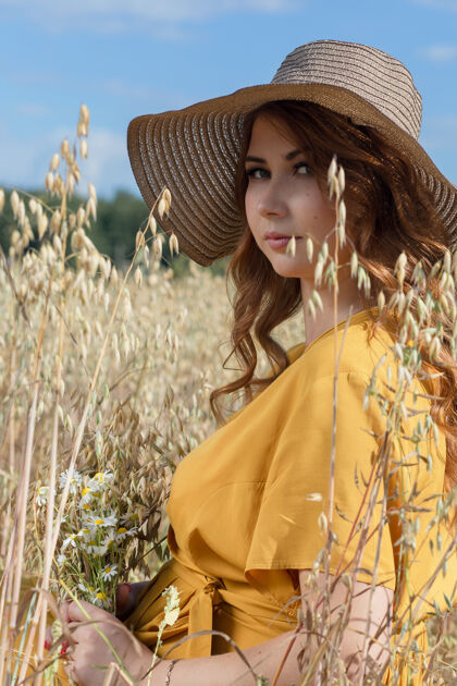 父母在一个阳光明媚的夏日 一位年轻漂亮的孕妇穿着黄色的裙子 戴着黄色的帽子 走过一片麦田女性农场太阳