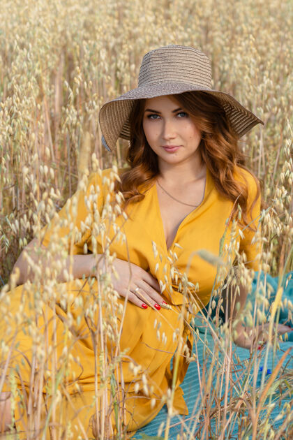 温暖在一个阳光明媚的夏日 一位年轻漂亮的孕妇穿着黄色的裙子 戴着黄色的帽子 走过一片麦田麦田农业出生